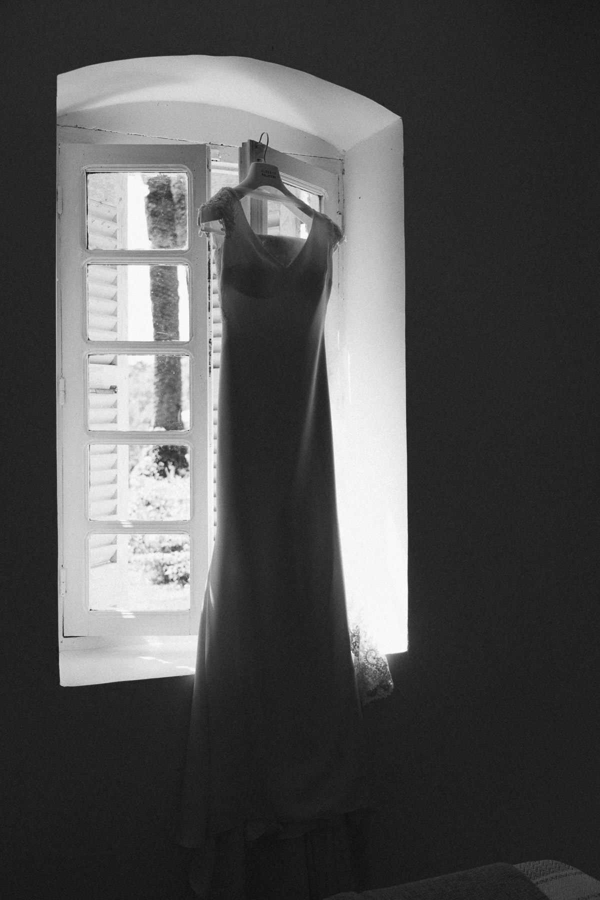 Robe de mariée suspendue devant une fenêtre au Domaine de Vignale en Corse